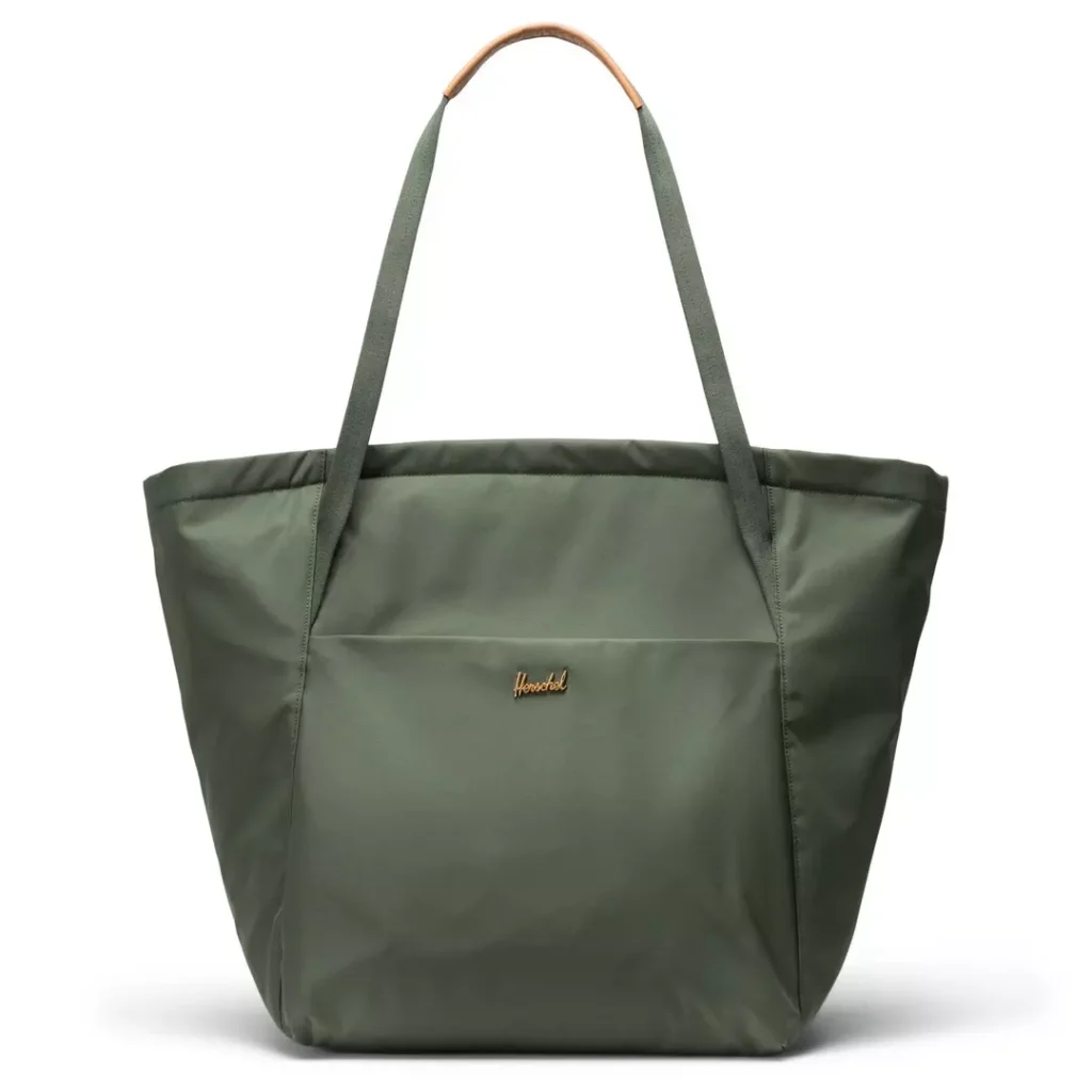 dark green Herschel tote bag with top shoulder handles and a large drop-in front accessories pocket, plus a small metal Herschel logo badge at the pocket