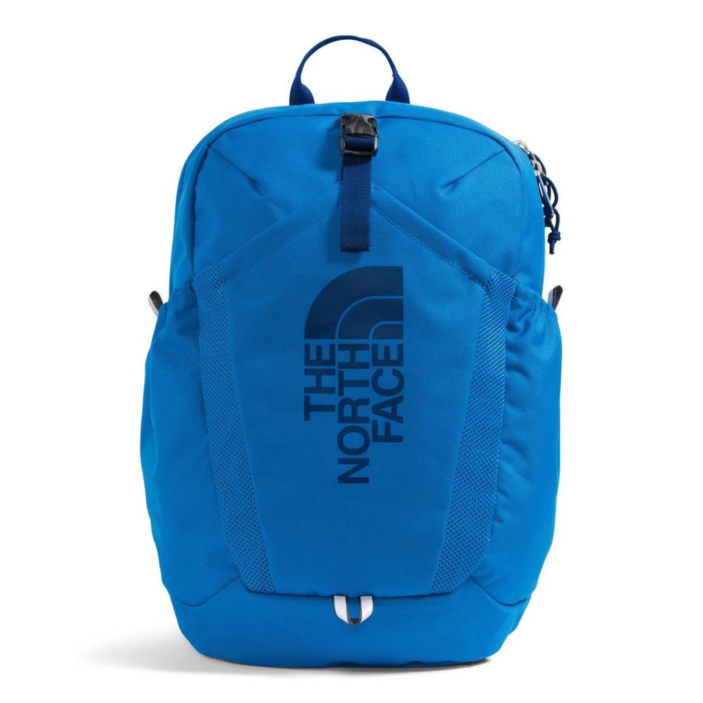 blue backpack with a top carry handle and a large darker blue/navy graphic at the front featuring The North Face half dome logo; there are deep side pockets visible, as well as a zippered main compartment and a front pocket with buckled webbing strap