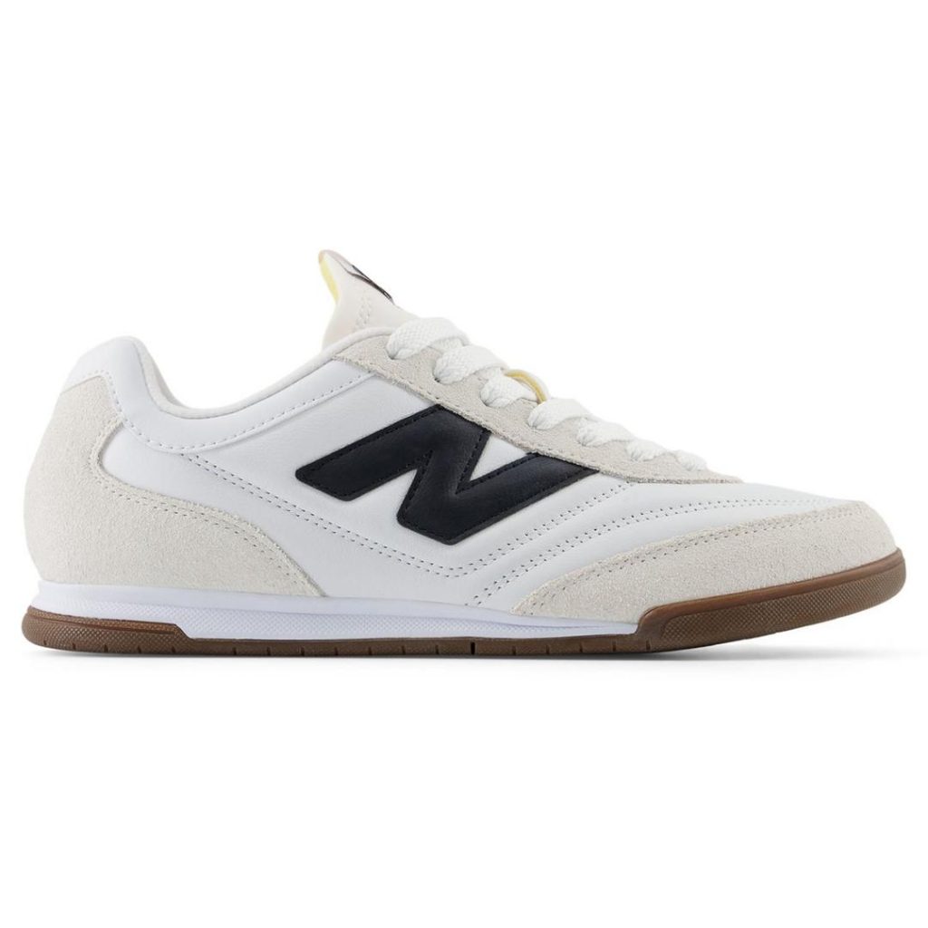 Tonal white and off-white New Balance low-profile sneakers with an angled "N" logo at the side in dark midnight blue/blackish colour. White laces on top. Contrast dark brown gum rubber along the outsole.