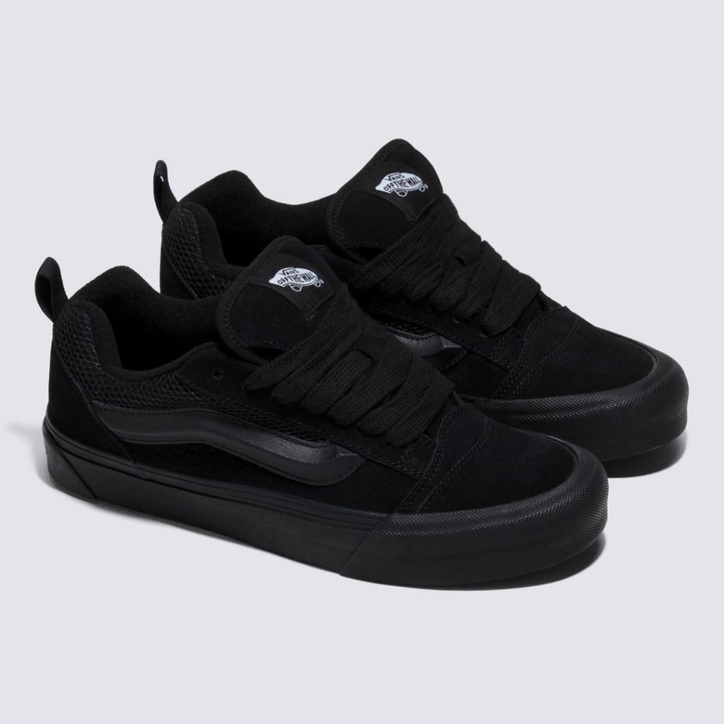 All black low-top Vans shoe with a black rubber outsole that wraps up and around the entire bottom of the shoes. Tonal black details with contrast black trim at the Vans sidestripe logo at the side. Black laces at the top and a black heel pull loop. White woven Vans logo patch at the tongue.