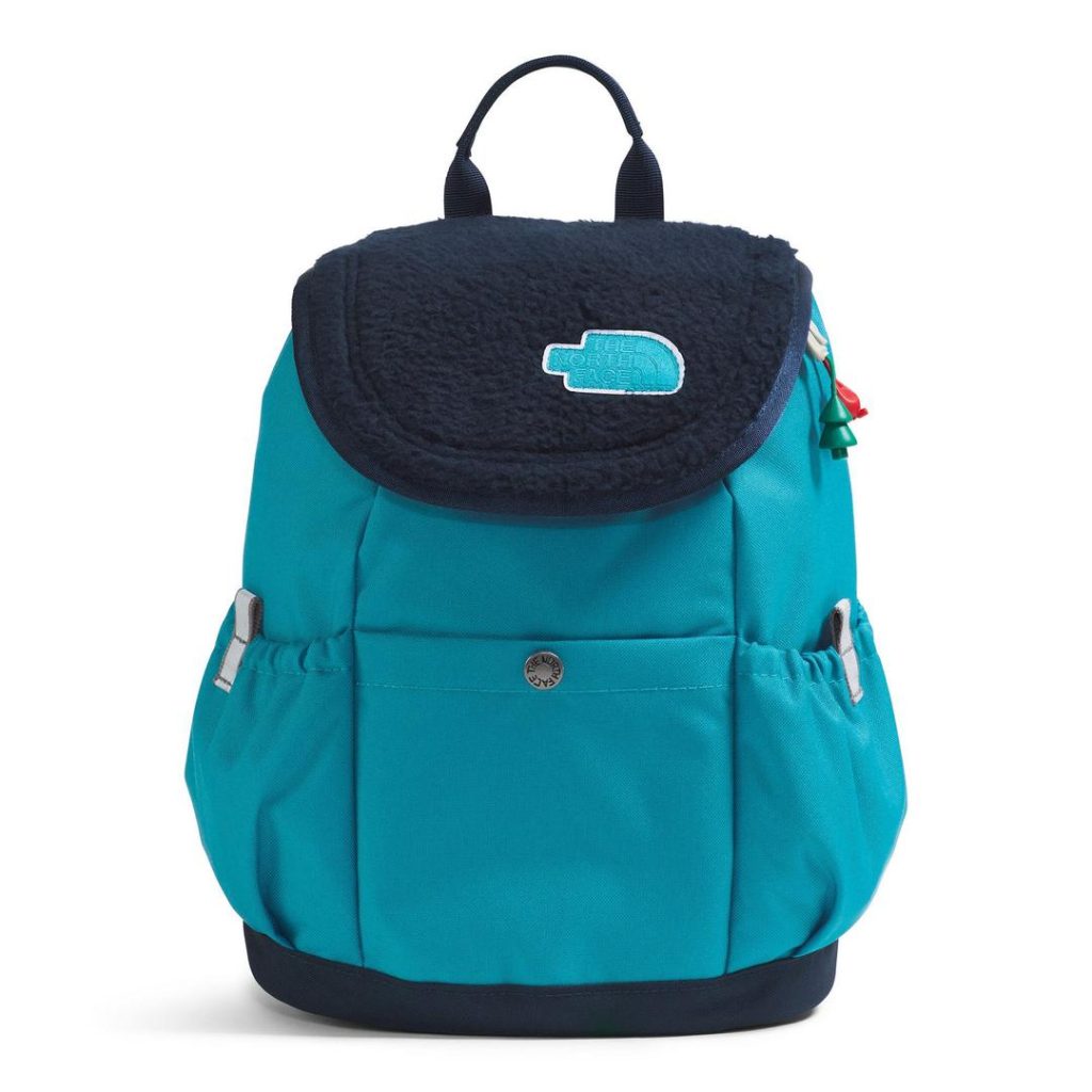small blue canvas backpack with a darker blue/navy fleece fabric flap and a darker blue/navy base and top carry handle; it has stretchy side water bottle pockets with an open-top drop-in snap button pocket at the front; the fleece flap includes a blue logo patch with The North Face's half dome logo