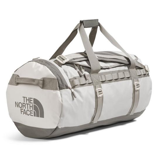 off-white The North Face duffel bag with contrast taupe/grey webbing trim, top carry handles and base; includes webbing daisy chain lash points along the side, a haul handle on the top and a crossbody/shoulder strap tucked between the carry handles, plus "The North Face" half dome logo at the side; gym class essentials