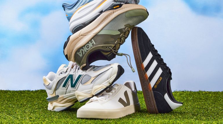 a stacked pile of New Balance, Veja, adidas, HOKA shoes with 5 in total; against a blue sky on green grassy ground